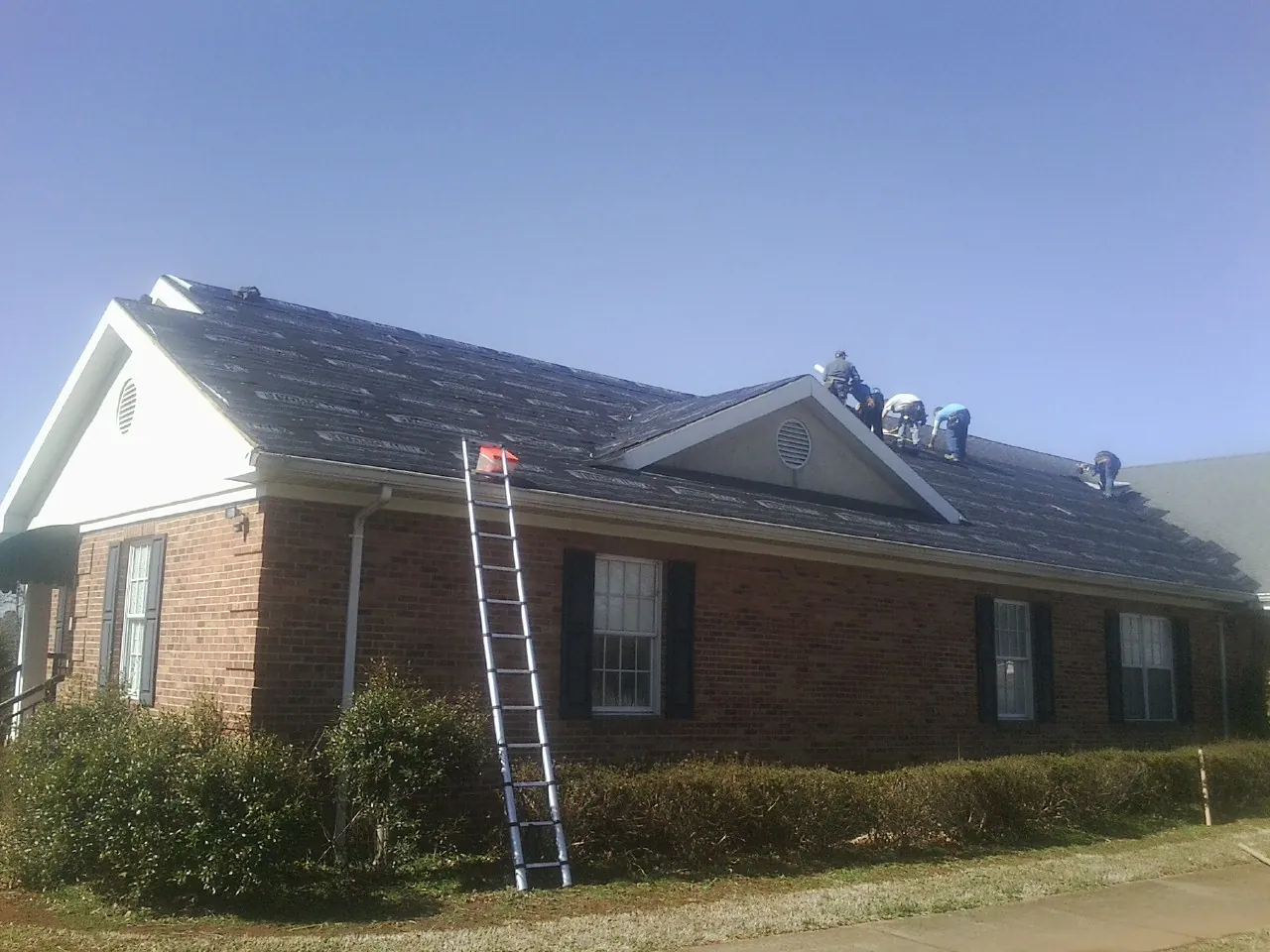 Crew tearing shingles off a brick ranch roof with a ladder set — Emergency Roof Repair work by our crew in East Windsor