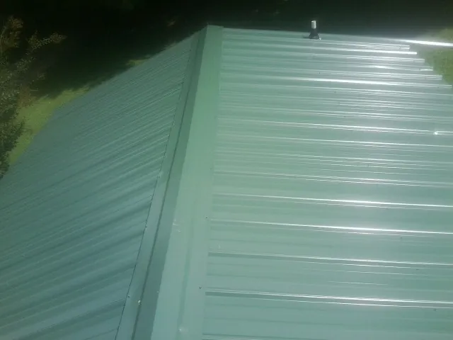New green metal panels meeting at the ridge of a roof — Flat Roof Repair work by our crew in East Windsor