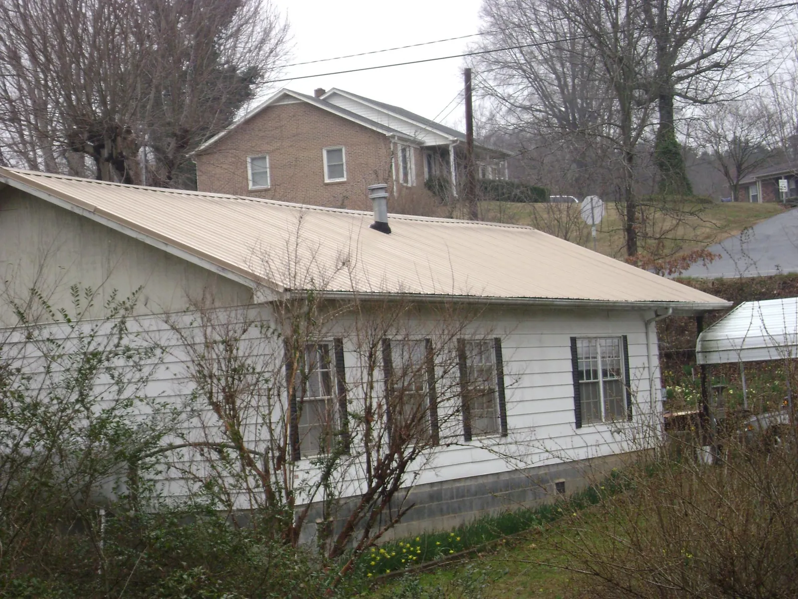 Tan metal roof on a white sided house set into a hillside — Commercial Roofing by Roofing Brothers in East Windsor